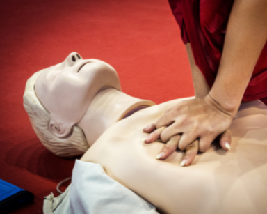 Person performing CPR on a mannequin with a red background